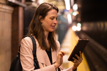 Business woman in city using tablet computer on subway platform