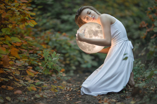 Beautiful attractive girl in a white dress in the autumn forest, hugs the moon, a mystery, a mysterious forest, artistic photography, with space