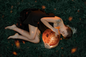 Beautiful attractive girl in a black dress embraces the planet Venus, a riddle on the grass, artistic photography, top view