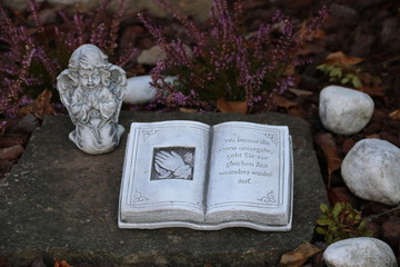Grabschmuck mit Engel und Buch auf dem Friedhof neben Blumen im Herbst