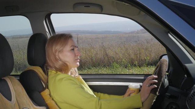 Confident young woman drinks coffee at the wheel of a car. slow motion