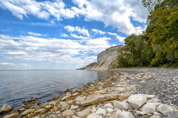Chalk cliffs above the still water.Boulders and pebbles in the foreground and clouds in the blue sky
