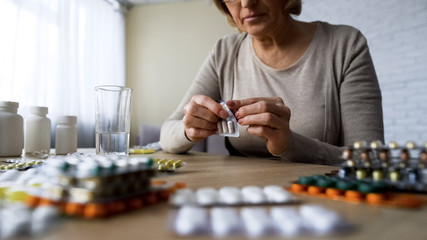 Unhealthy elderly lady drinking pills, vitamins, illness symptoms, hypochondria