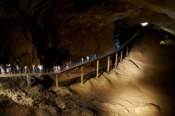 underground cave excursion. big group of tourists at bridge in the darkness. New Athos Caves, Abkhazia
