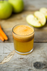 Homemade fresh squeezed apple and carrot healthy juice in a clear glass with apple and carrot on a side
