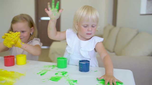 Happy family paints colors. Happy little childs making colorful color handsprint on the white paper. A little cute happy funny girls painting color with smiling mother together. Slow motion