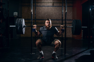 Muscular caucasian bearded man lifting weights and doing back squat in gym.