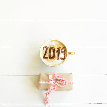 New Year 2019 is written on a cup of coffee with milk. The concept of the new year on January 1. On a white background with a gift