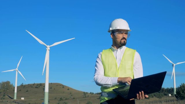 Green energy concept. A man looks at wind turbines and types on his laptop. 4K
