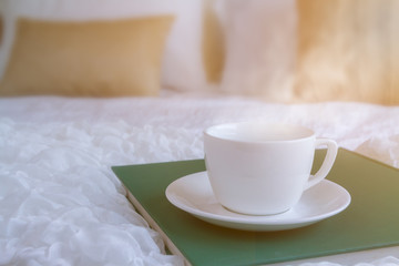 White coffee cup put on green plate in the bed room with soft streme smoke and window lighting. Background process by sunlight effect as a morning. Selective focus and copy space