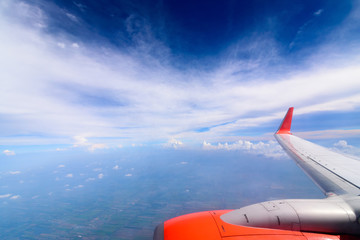 View of the wing of airplane with  blue sky and white cloud on high level. Beautiful sunset sky clouds  seeing through the airplane window.