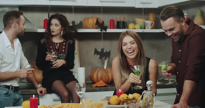 Two beautiful couples have a funny time on Halloween party , they have conversation, holding a glass with wine and cocktails, beautiful Halloween decorations around.