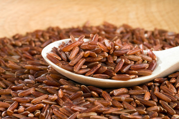Brown unpeeled rice on a wooden spoon against a blurred background.