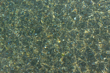 Shimmering sun glares on pebble seabed under water as background.