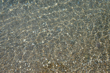 Shimmering sun glares on pebble seabed under water as background.