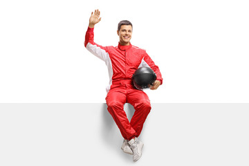 Race driver sitting on a panel and waving at the camera