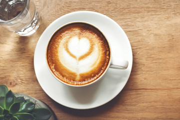 Cup of cappuccino with latte art on wooden background with plant. Hot coffee with flower on table. Top view, flat lay copy space for text. Beautiful foam, top view, copy space.