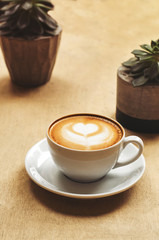 Cup of cappuccino with latte art on wooden background with plant. Hot coffee with flower on table. Top view, flat lay copy space for text. Beautiful foam, top view, copy space.