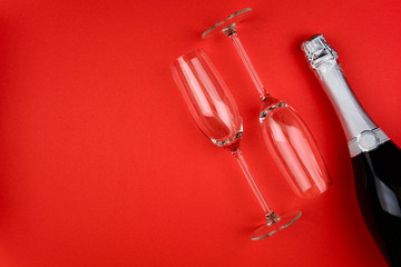 Wineglasses and bottle of champagne lying on red paper background. New Year celebration concept. Top view. Flat lay. © thayra83