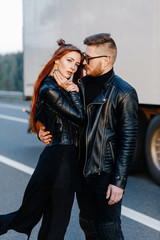 Fototapeta na wymiar red skinny girl in a black dress stands together with the bearded guy on the highway