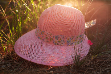 straw hat with a ribbon on flower field background. Warm sunset light beams