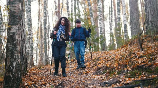 Young woman and a boy on scandinavian walk in the forest. Going downhill.