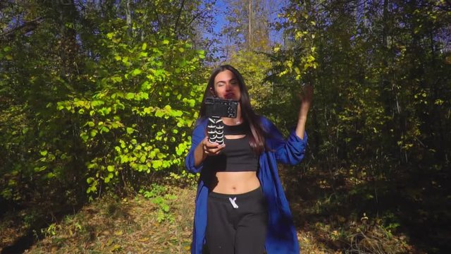 Brunette young woman blogger going in forest and recording video for vlog using camera slow motion