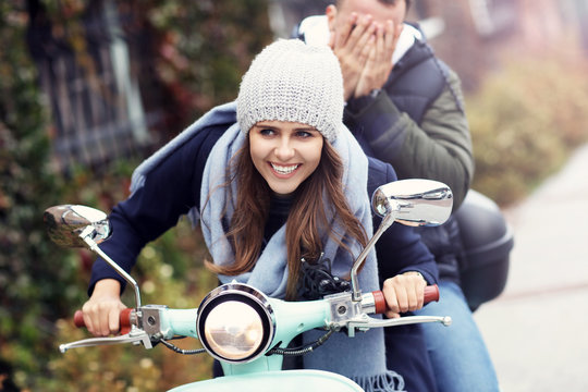 Beautiful young couple smiling while riding scooter in city in autumn