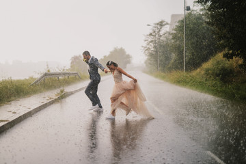 Silly young just married couple crossing road on rainy day. Running in wet ceremonial clothes.