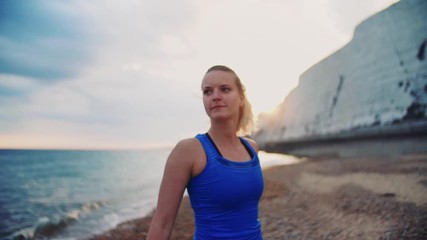 Young sporty woman runner in blue sportswear walking on the beach outside.