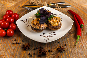 Stuffed mushrooms and greens on a white plate. nearby are pepper, cherry tomatoes and Cutlery
