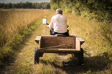 farmer man in work clothes riding on a motor-block with a trailer