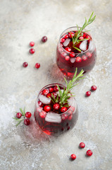 Cold refreshing drink with cranberries and rosemary on a gray concrete background