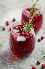 Cold refreshing drink with cranberries and rosemary on a gray concrete background