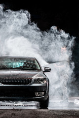 A man with a beard or car washer washes a gray car with a high-pressure washer at night in a shop wash