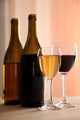 A glass of white wine and a glass of red wine next to bottles of