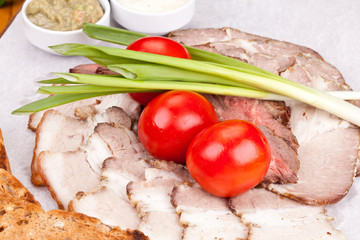 Assorted cold meat with toasted bread, cherry tomatoes, onion and sauces on white plate. Close up