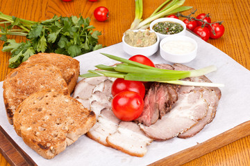 Assorted cold meat with toasted bread, cherry tomatoes, onion and sauces on white plate. Close up