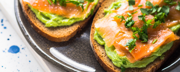Rye bread avocado toasts with smoked salmon on white wooden board
