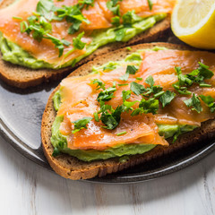 Rye bread avocado toasts with smoked salmon on white wooden board