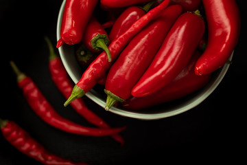 Red chili peppers in a plate on a dark background, top view
