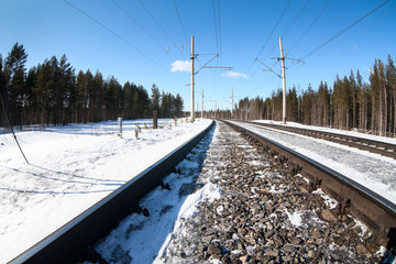 Electrified railway line among wintry forest at sunny day, close-up view at rail-track