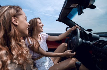 smiling girlfriends traveling in a convertible car.