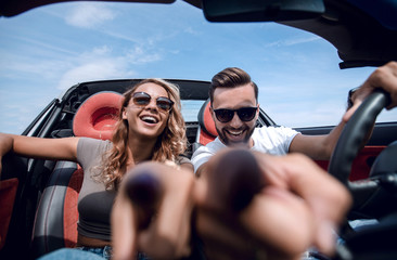 close up.young couple sitting in a convertible and pointing at y - obrazy, fototapety, plakaty