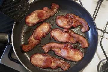 Bacon fried burnt crispy breakfast in pan on cooker hob view from above