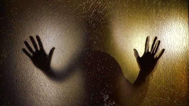 ghost female figure is moving behind transparent glass screen, standing her hands on it and looking