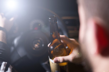 Drunk young man driving a car with a bottle of beer. Don't drink and drive concept. Driving under the influence. DUI, Driving while intoxicated. DWI
