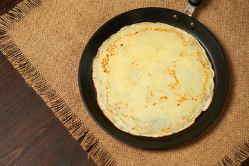 Crepe closeup, thin pancake on a frying pan, wood background