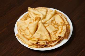 Crepe closeup, heap of thin pancakes on a dish, wood background