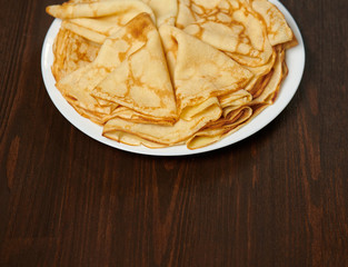 Crepe closeup, heap of thin pancakes on a dish, wood background